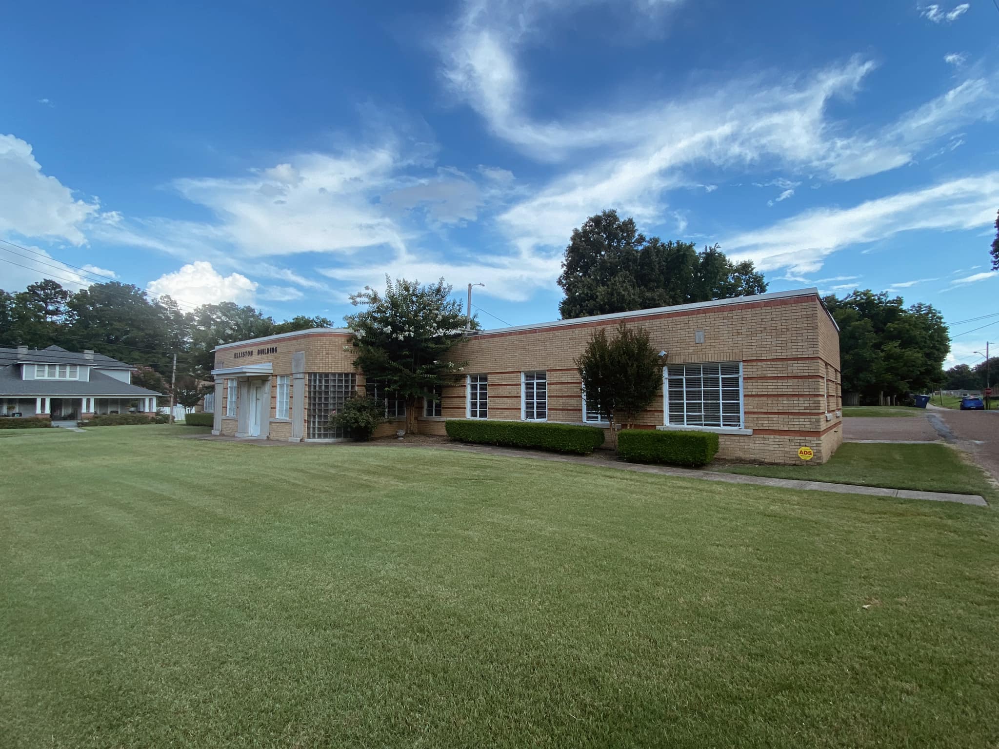 A photo of the exterior of the Tipton County Carl Perkins Center, a brown brick building with six red accent stripes across the building, a white door and awning, and several bushes and small trees around the outside.