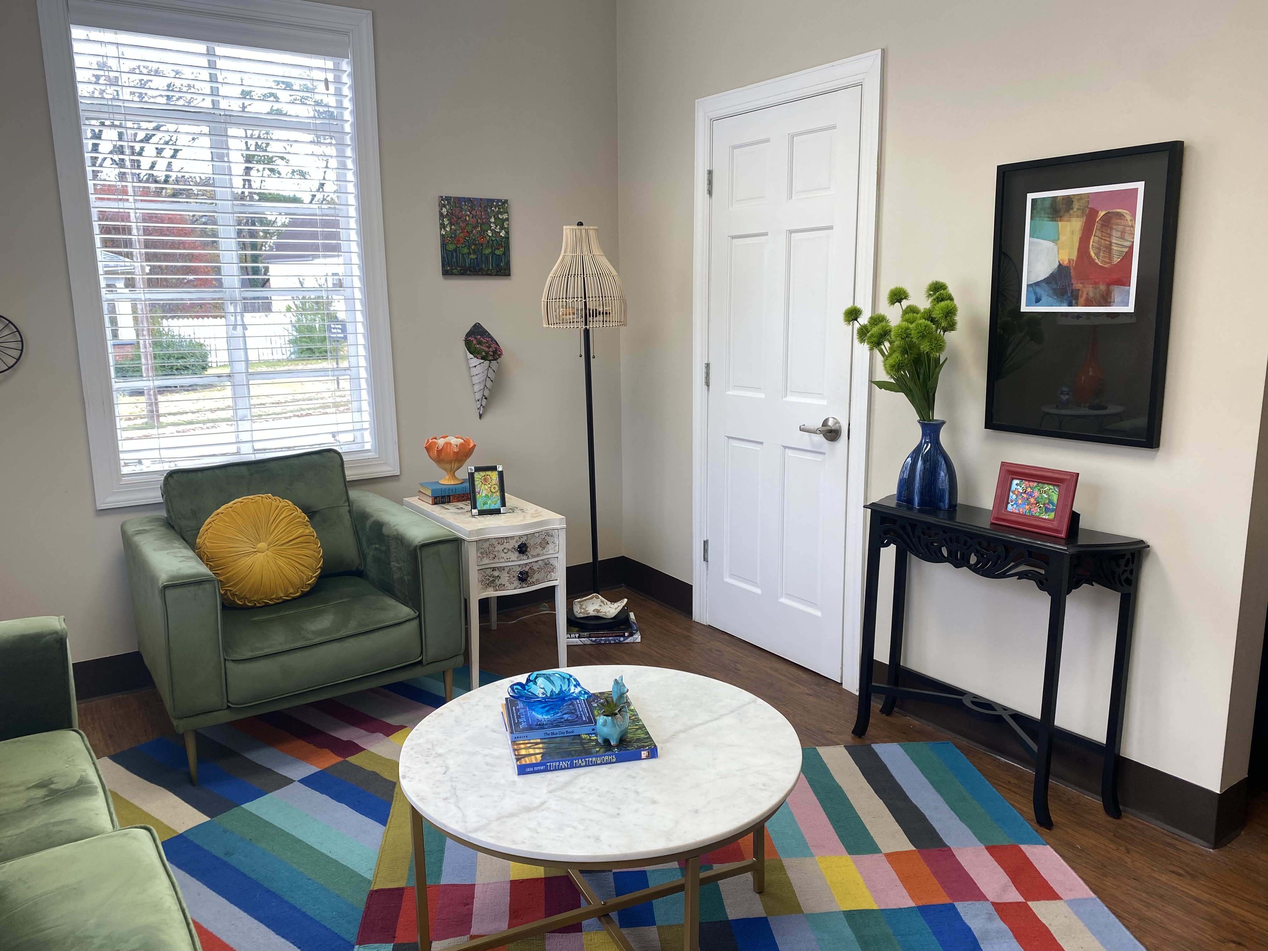 The other side of the room in the previous image, with the green chair and yellow cushion on the left, a window behind the chair, a closed door on the right wall and several pieces of decor on the walls and floor